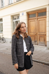 a lady in a white ruffle collared shirt, a sequin tweed jacket and a pair of black shorts